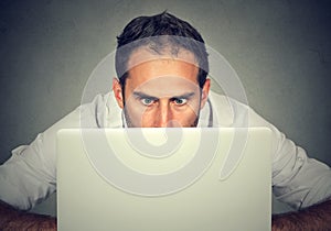 Man hiding behind a laptop staring at screen with a shocked face expression