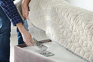 Man hiding dollar banknotes under mattress in bedroom. Money savings