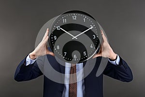 Man hiding face behind clock on dark background. Time management concept