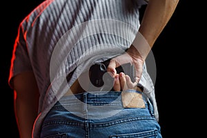 Man hiding his gun in his jeans on black background