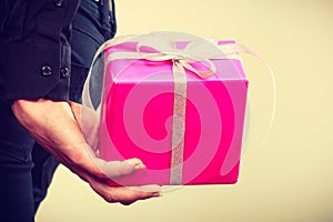 Man hiding pink gift box with ribbon behind back