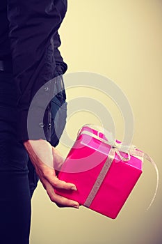 Man hiding pink gift box with ribbon behind back