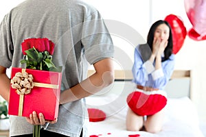 Man hiding red gift box with beautiful red rose bouquet behind back, ready to give Valentine present to lover girlfriend for