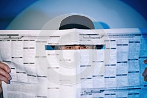 Man hiding watches through the newspaper in the spotlight on studio background