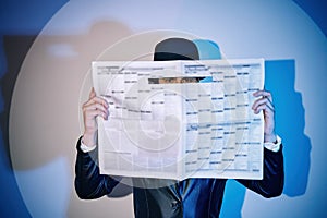 Man hiding watches through the newspaper in the spotlight on studio background