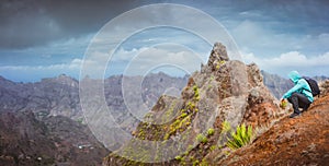 Man hiker with backpack sitting on the mountain top and looking down to the valley. Stunning arid landscape on Santo