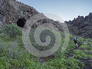 Man hiker at footpath of hiking trail Tasartico to Playa GuiGui beach, Barranco de Guigui Grande ravine with cacti