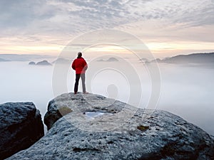 Man hiker at mountain peak. Marvelous daybreak in autumn misty landscape. Sun hidden in clouds