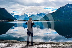 Man hiker photographs beautiful landscape of mountains reflected in Romsdal Fjord or Romsdalsfjord in cloudy weather. Andalsnes.