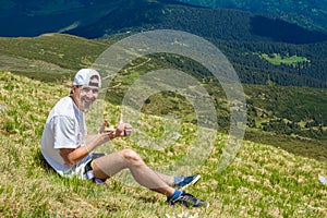 Man hiker relaxing on top of hill and admiring beautiful mountain