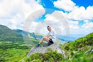 Man hiker relaxing on top of hill and admiring beautiful mountain valley view