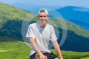 Man hiker relaxing on top of hill and admiring beautiful mountain valley view