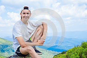 Man hiker relaxing on top of hill and admiring beautiful mountain valley view