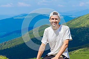 Man hiker relaxing on top of hill and admiring beautiful mountain valley view