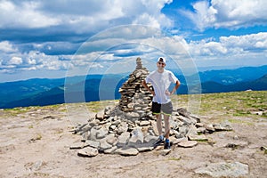 Man hiker relaxing on top of hill and admiring mountain valley view in summer day