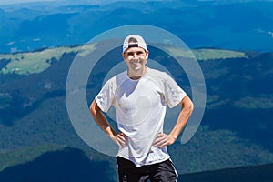 Man hiker relaxing on top of hill and admiring mountain valley view in summer day