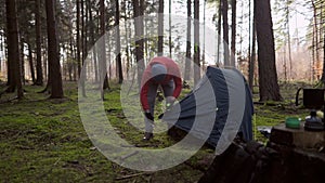 Man hiker sets up camping tent in the fall forest on backpacking expedition. Traveler setting an overnight tent in the