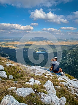 Man Hiker Sitting with Dog on Mountain Top