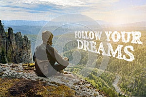 Man hiker sitting on top of mountain and contemplates beautiful view to the valley. Follow your Dreams lettering.