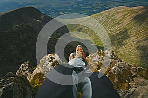 Man hiker sitting on the top of mountain rocks. Beautiful weather with Scotland nature. Detail of hiking boots on the difficult pa