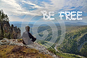 Man hiker sitting on top of mountain and see a sign on sky. Lettering Be Free. Freedom concept