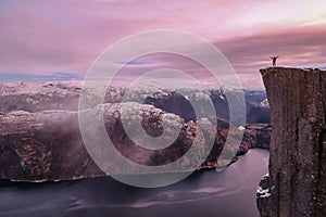 Man hiker standing on the famous Preikestolen over the Lysefjord, beautiful colors at sunset, Ryfylke, Rogaland, Norway