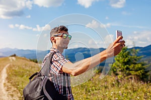 Man hiker taking selfie with smartphone in Carpathian mountains on hill peak. Traveler backpaker enjoys view photo