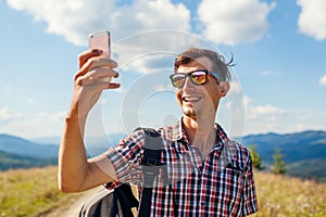 Man hiker taking selfie with smartphone in Carpathian mountains on hill peak. Traveler backpaker enjoys view photo