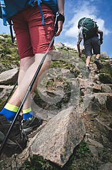 Man hiker walking on mountain rocks with sticks. Beautiful weather with Scotland nature. Detail of hiking boots on the difficult p