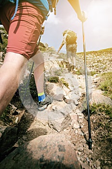 Man hiker walking on mountain rocks with sticks. Beautiful weather with Scotland nature. Detail of hiking boots on the difficult p