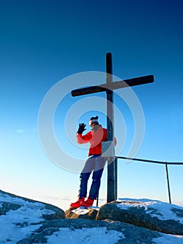 Man hiker in warm clothes on summit with wooden cross.