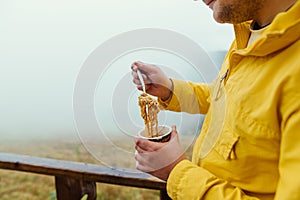 Man hiking in the mountains eating pasta from a cup, close-up photo of breakfast in the mountains