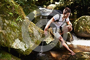 Man, hiking and river in tropical jungle with smile for adventure, journey and rocks with backpack. Person, outdoor and