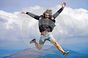Man hipster jumps on mountain top on cloudy sky.