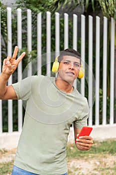 man in his 20's laughing wearing headphones showing the victory sign