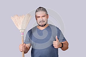 A man in his 30s holding an old broom. A househusband doing the the house cleanup. Cleanliness concept