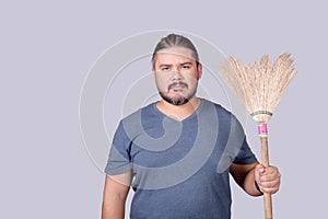 A man in his 30s holding an old broom. A househusband doing the the house cleanup. Cleanliness concept