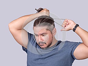 A man in his 30s ties his long hair into a ponytail with an elastic band. A guy in a gray shirt fixing his messy hair. Isolated on