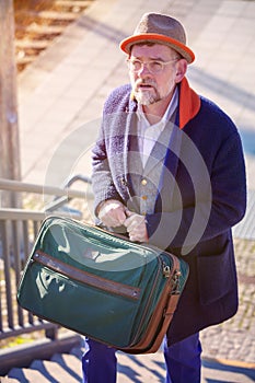 Man in his 50s walking with suitcase up stairs at train station