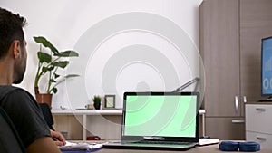 Man at his desk in front of computer with green screen