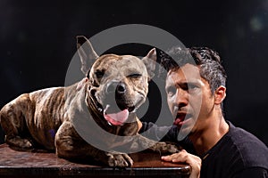 a man and his dog stick out their tongues. isolated black background. pitbull latin man