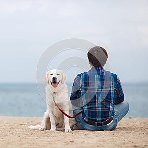 Man with his dog at the summer beach sitting back to camera