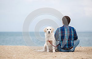 Man with his dog at the summer beach sitting back to camera