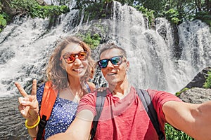 Man and his girlfriend take a selfie against the backdrop of a picturesque waterfall in a nature park. The concept of travel