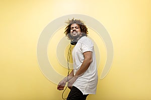 A man with his hair in a frizz and headphones on the neck is dancing with a bliss expression on the face over the yellow