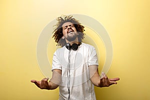 A man with his hair in a frizz and headphones on the neck is holding his hands in front of him and making a horn gesture