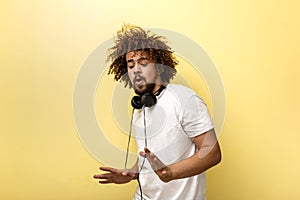 A man with his hair in a frizz and headphones on the neck is holding his hands tensed in front of him and looking