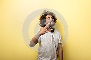 A man with his hair in a frizz and headphones on the neck is standing with his hand in front of him and making a `Vulcan