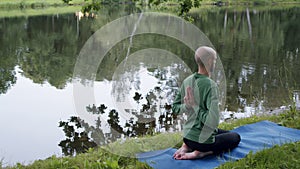 A man with his hands behind his back is engaged in spiritual practice on the banks of a river or lake in unity with