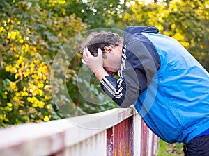 Man with his head in his hands and leaning on the railing, worried and sad